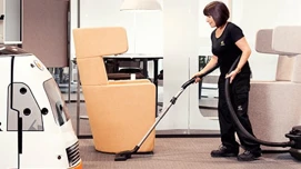 Rengøringsmedarbejder der støvsuger i et åbent kontorområde