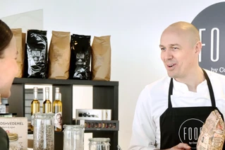 Kvinde taler med smilende kok i moderne café med FOOD by Coor logo.