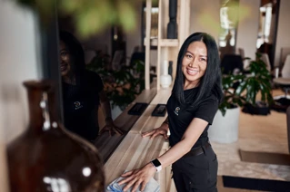 Glædelig kvinde med logo-t-shirt ved receptionen i moderne kontormiljø.