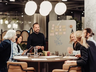 Et team af professionelle holder brainstormmøde rundt om konferencebord i moderne kontormiljø.
