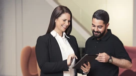 To kvinders kollegaer diskuterer arbejde på en tablet i et moderne kontormiljø.