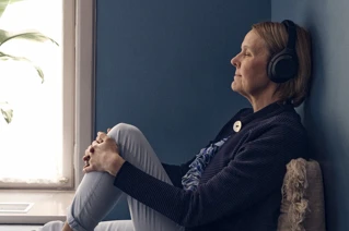 Kvinde nyder musik i hovedtelefoner ved vindue med plante