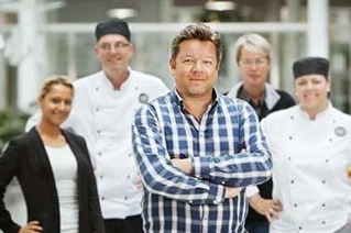 Gruppe af professionelle kokke og restauratører med krydsede arme står foran restaurantinteriør i Danmark.