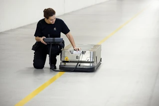 Kvinde betjener en automatiseret logistikrobot i et lagermiljø.