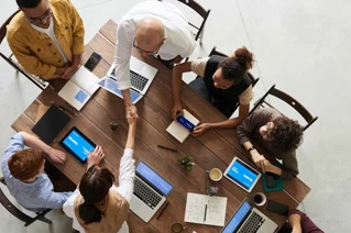 Gruppe af medarbejder der alle sidder med en computer foran sig, mens to af medarbejderne giver hånd