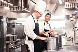 To kokke smiler og arbejder sammen i et professionelt køkken.